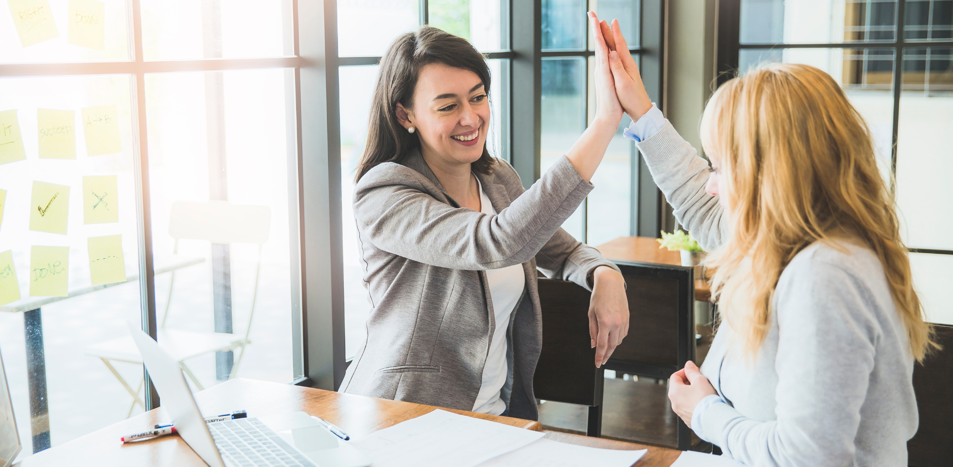 Zwei Frauen in Businesskleidung geben sich einen High Five.