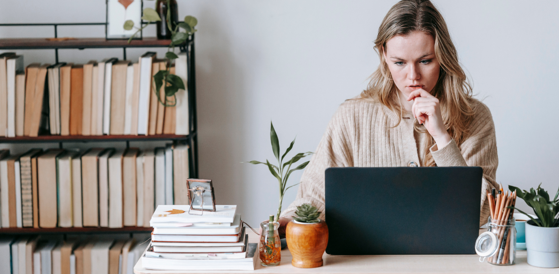 Nachdenkliche Frau sitzt am Schreibtisch vor dem Laptop.