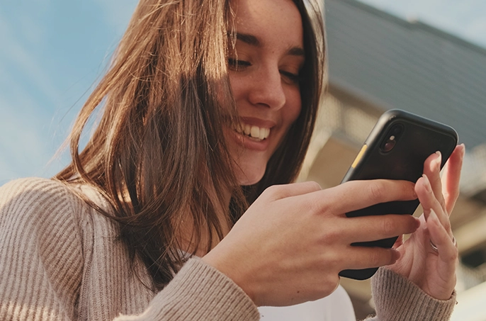 Eine junge Frau schaut interessiert auf ihr Smartphone und freut sich.