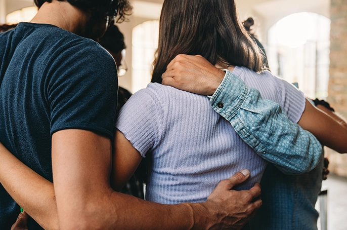 Eine Gruppe von Personen steht eng in einer gemeinsamen Umarmung im Kreis zusammen.