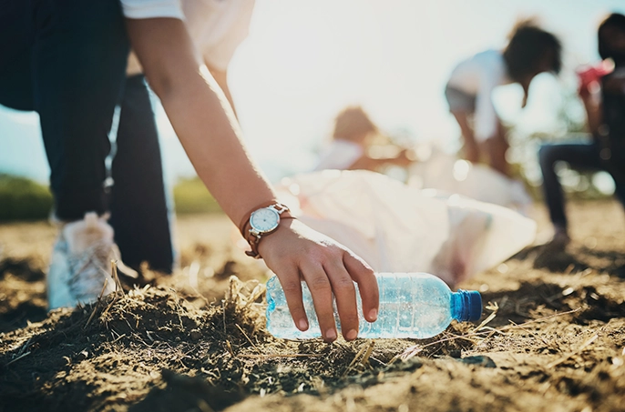 Close up auf die Hand einer Sport treibenden Person im Freien, die eine Wasserflasche am Boden aufhebt.