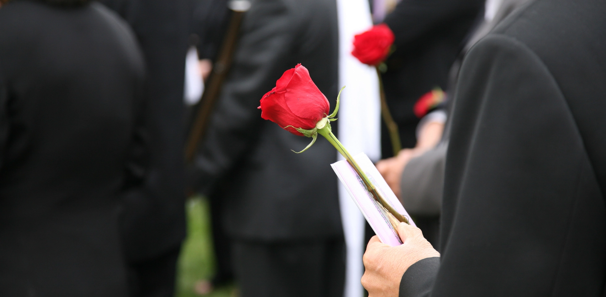 Ein Mann steht bei einer Trauerfeier mit einer roten Rose in der Hand.